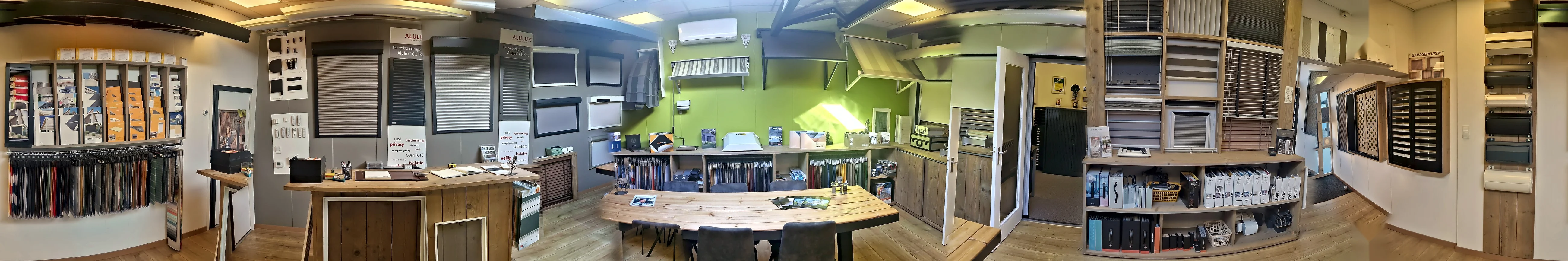 Showroom van ZBN rondom: folderrek met doekstalen, de toonbank, de wand met rolluiken en screens, de groene wand met zonneschermen, de kast met binnenzonwering en de wand met garagedeuren