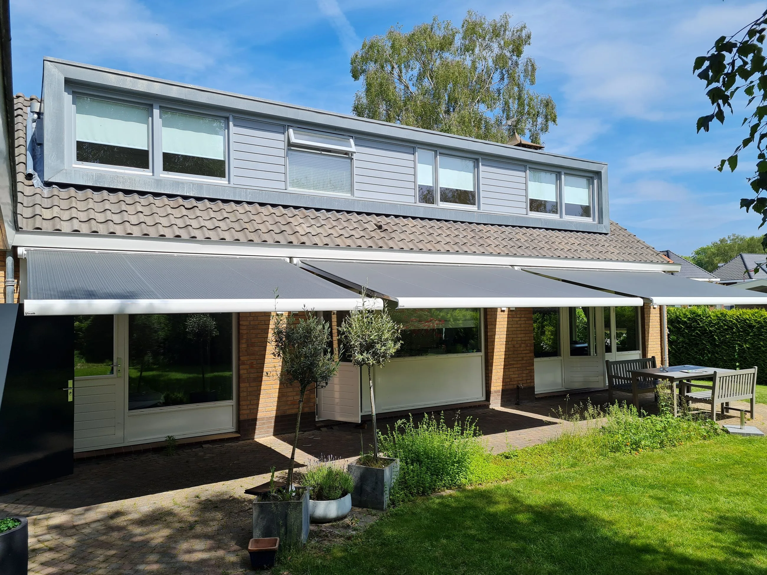 Drie grijze knikarmschermen naast elkaar aan de achtergevel van rijtjeswoningen